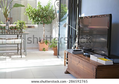 Still life view of a home living room with a flat screen TV, with a small terrace garden outdoors area, indoors and outdoors. Home entertainment technology, empty space, aspirational lifestyle.
