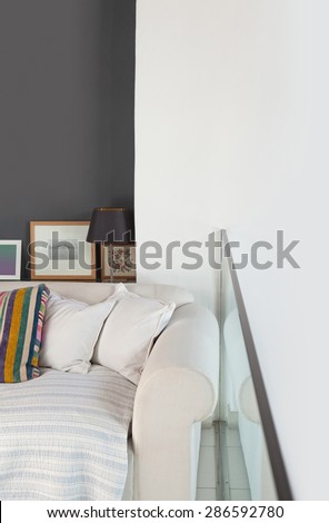 Still life home interior view of comfortable white sofa in stylish home living room with a modern glass banister, indoors. Elegant family room with photo frames, empty space, aspirational lifestyle.