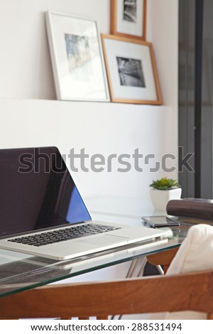 Still life view of a home office room with a laptop computer and a smart phone, house interior with photo frames. Working from home technology in a home work desk, indoors. Lifestyle workplace.
