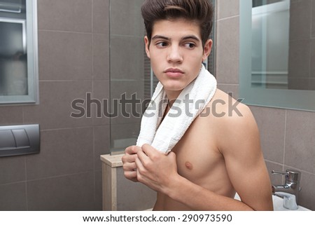 Beauty portrait of a young man in a home bathroom with a white towel around his neck, thoughtful, home interior. Health, care and well being male grooming, indoors. Man portrait with perfect skin.