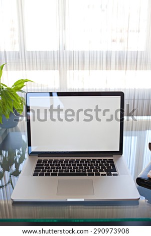 Still life view of office room with open laptop computer on glass desk with reflections by bright window, office interior with paperwork and plant. Professional home workplace, technology indoors.