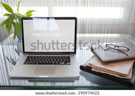 Still life view of office room with open laptop computer on glass desk with reflections by window, office interior with paperwork and spectacles. Professional workplace, technology indoors.