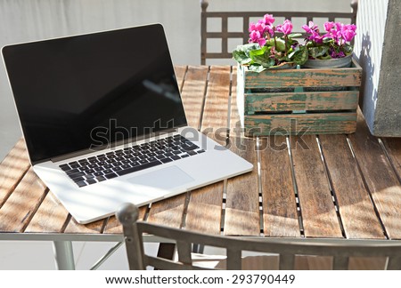 Still life view of open laptop computer on a terrace patio wooden table with decorative flower pot in home exterior area, outdoors. Technology at home and working from home environment with no people.