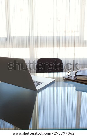 Still life view of an office interview room with an open laptop computer on a glass desk with reflections against window, office interior with paperwork. Professional workplace, technology indoors.