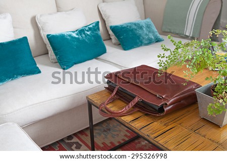 Still life of a luxurious living room with a white sofa and a bamboo coffee table with a quality leather briefcase with paperwork and folders, home interior. Aspirational house indoors lifestyle.