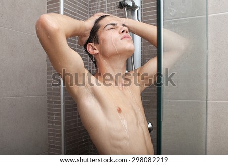 Portrait of adolescent young man washing his body skin and hair under a shower at home, bathroom interior. Healthy man lifestyle, well being and grooming. Teenager getting ready, indoors.