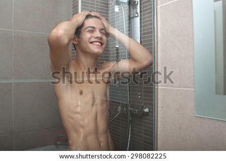 Portrait of an adolescent young man washing his skin and hair under a shower at home, bathroom interior. Healthy man lifestyle, well being and grooming. Teenager getting ready in the morning, indoors.