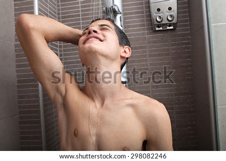 Portrait of an adolescent young man washing his body skin and hair under a shower at home, bathroom interior. Healthy man lifestyle, well being and grooming. Teenager getting ready, indoors.