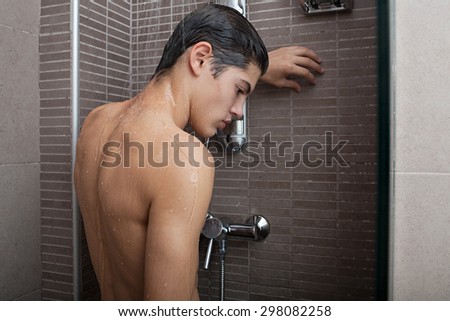 Rear view of adolescent young man washing his body skin and hair in a shower at home, bathroom interior. Healthy man lifestyle, well being and grooming. Teenager portrait getting ready, indoors.