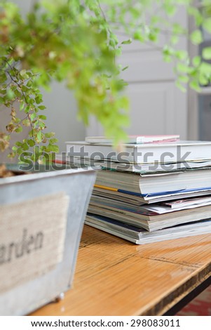 Still life detail of living room with a bamboo texture coffee table and a pile of books and magazines next to a green plant, home living room interior. Aspirational living space, indoors lifestyle.