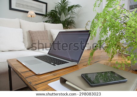 Still life detail of luxurious living room with photo frame, an open laptop computer and a smartphone with paperwork and folders, home living room interior. Aspirational technology indoors lifestyle.