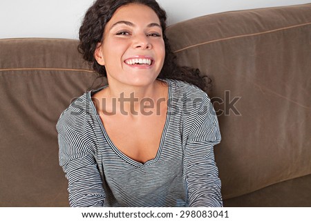 Beautiful and joyful young woman lounging on a comfortable sofa at home, having fun laughing and relaxing in living room interior. Positive home lifestyle, indoors. Girl fun expression, smiling.