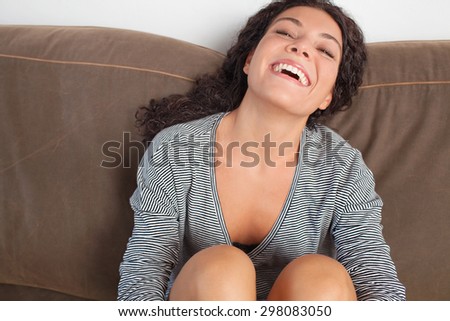 Portrait of beautiful young joyful woman lounging on a comfortable sofa at home, laughing and relaxing in living room interior. Positive expression home lifestyle, indoors. Girl joyfully smiling.