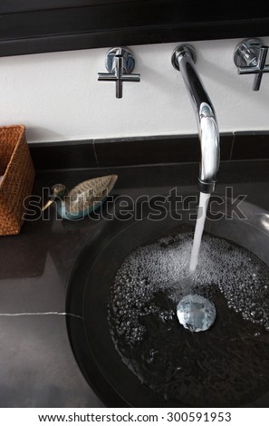 Still life view of a quality luxurious bathroom with a black marble sink in an exclusive bachelor home with water running from tap, bath interior. Masculine hotel bathroom for travelers, indoors.