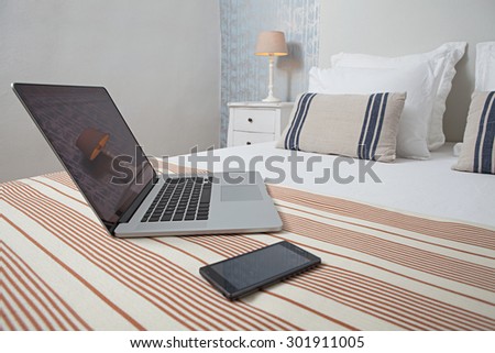 Still life view of a luxury hotel bed in an elegant home interior with an open laptop computer and a smartphone mobile phone. Comfortable accommodation for business travelers, bedroom with technology.
