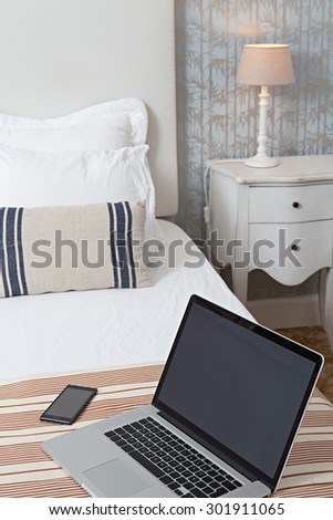 Still life view of a luxury hotel bed in an elegant home interior with open laptop computer and a smartphone mobile phone. Comfortable accommodation for business travelers, bedroom with technology.