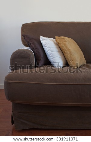 Still life view of a family home living room with a comfortable brown sofa with cushions in a wooden floor house interior, against a white wall. Home relaxing and lounging space, simplicity, indoors.