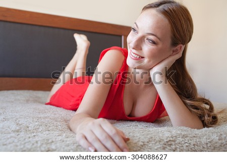 Portrait of a beautiful young woman laying down on her bed at home, leaning and relaxing in her bedroom, smiling indoors. Aspirational lifestyle and beauty, interior.