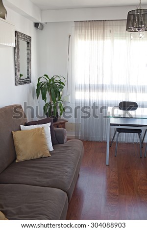 Still life view of a family home living room with a comfortable brown sofa with cushions in a wooden floor house interior with large window and curtains. Home relaxing space, indoors.