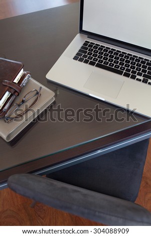 Still life view of a male office desk with an open laptop computer on wooden desk, professional office interior, paperwork and chair. Professional workplace with reading glasses, technology indoors.