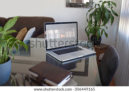 Still life of a home office living room with open laptop computer on a glass desk, professional office interior with paperwork and chair. Working from home professional workplace, technology indoors.