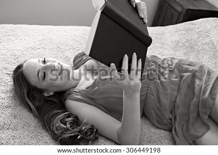 Black and white portrait of young student woman laying on a bed at home smiling, reading a book, lounging and relaxing. Girl beauty reading in home bedroom, indoors lifestyle, house interior.