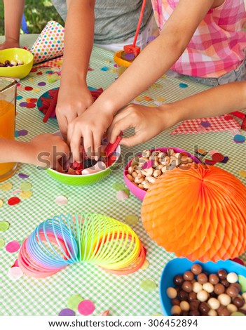 Detail of four children hands taking sweets and party food at a home garden birthday party having fun, outdoors. Kids celebrating, eating and enjoying a colorful party on sunny day, lifestyle.