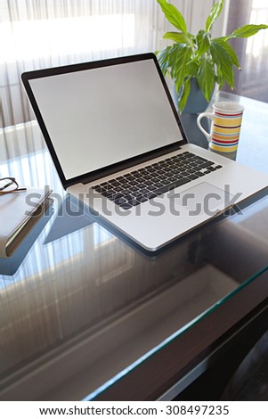 Still life view of an apartment living room with an open laptop on a professional glass desk workplace by a large bright window, interior. Home office technology, indoors. Working from home lifestyle.