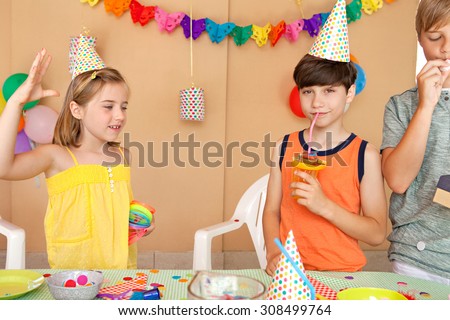 Group of kids celebrating a birthday party with a table full of food, sweets and fruit juices in a home garden party, outdoors. Children friends and family enjoying playing together, home exterior.