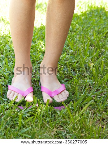 Detail view of a girl child feet wearing a pair of humorous fun pink sandals with grass sole, standing on green grass in home garden with wet skin on a summer holiday. Kids active lifestyle outdoors.