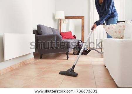 Faceless middle section of young woman using vacuum cleaner in home living room floor, doing cleaning duties and chores, meticulous interior. Young female working on house spring cleaning, indoors.