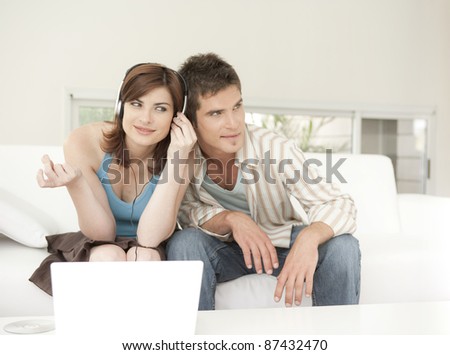 Man and woman using a laptop and listening to headphones at home.