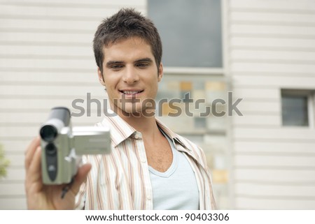 Man using a digital video camera outside his house.