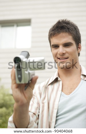 Young man using a digital video camera in office garden.