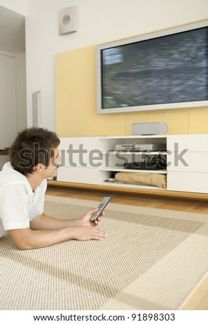 Young professional using a tv remote control while watching a flat screen tv at home.