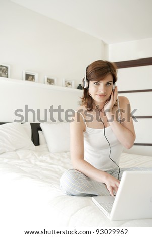 Young woman listening to music in bed, using a laptop computer and headphones.