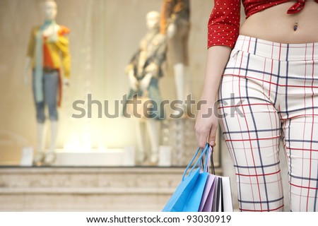 Close up of a young woman\'s body holding shopping bags, standing by shop window.