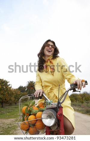 Elegant young woman riding a motorbike in an orange grove.