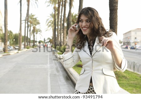 Attractive young woman talking on the phone in a tree aligned street.