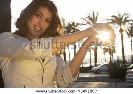 Portrait of a young woman holding the sun in her hands, with sun rays filtering through.