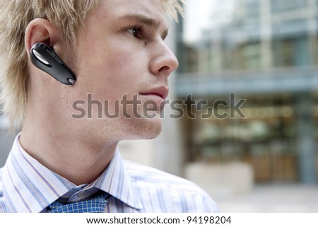 Close up of a young businessman using a hands free device to speak on his cell phone, exterior.