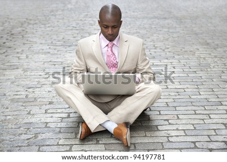 Young businessman using a laptop computer while sitting in the middle of the road.
