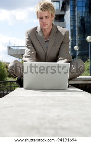 Businessman sitting down by an office building, using his laptop.