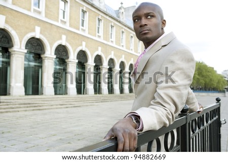 Businessman leaning on a banister, standing by a classic office building.