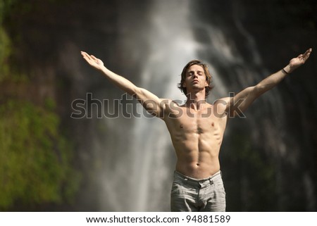 Attractive man standing by waterfalls with arms outstretched in the air.