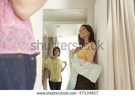 Two friends trying clothes on in a fashion store\'s fitting room.