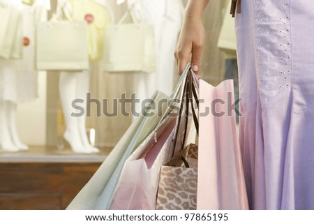 Detail close up of a woman\'s hand holding shopping bags by fashion store.
