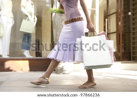 Detail of a young woman\'s body walking down a shopping street holding shopping bags.