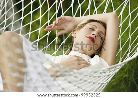 Attractive blonde woman laying down on a white hammock, sleeping and wearing red lipstick.