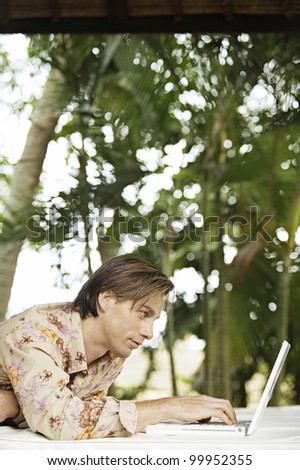 Young man using a laptop computer in a tropical garden while on vacation.